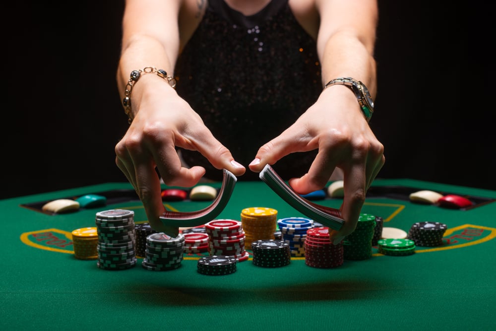 female croupier shuffling cards on poker table with chips