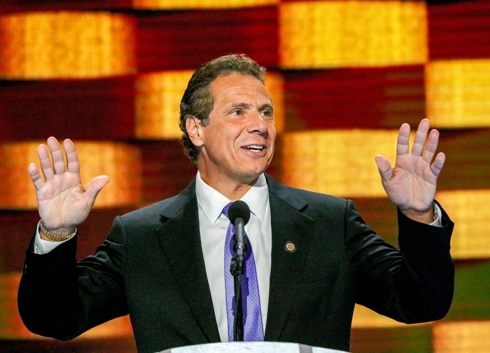 New York Governor Andrew Cuomo holds hands up while addressing a conference