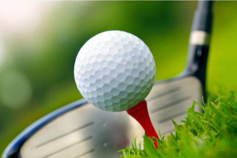 closeup of golf club head next to ball on tee